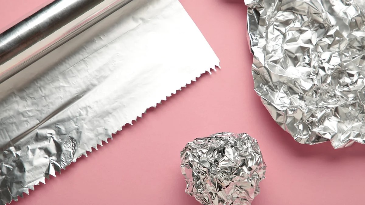 aluminiumfolie op een rol en tot een prop gekreukeld op een roze achtergrond